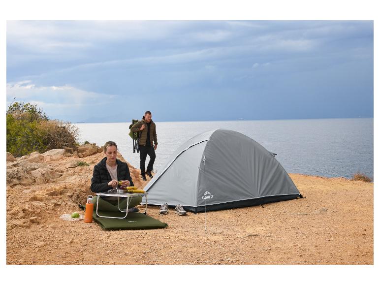 Tente de camping Crivit et femme préparant un repas en plein air au bord de la mer.