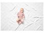 Un bébé dans un body rose sur une couverture blanche.