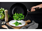 Brocoli cuit versé d'une poêle dans une assiette, avec moulin à poivre et plante.