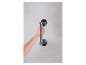 Une main féminine tient une poignée de douche en métal fixée à un mur gris.