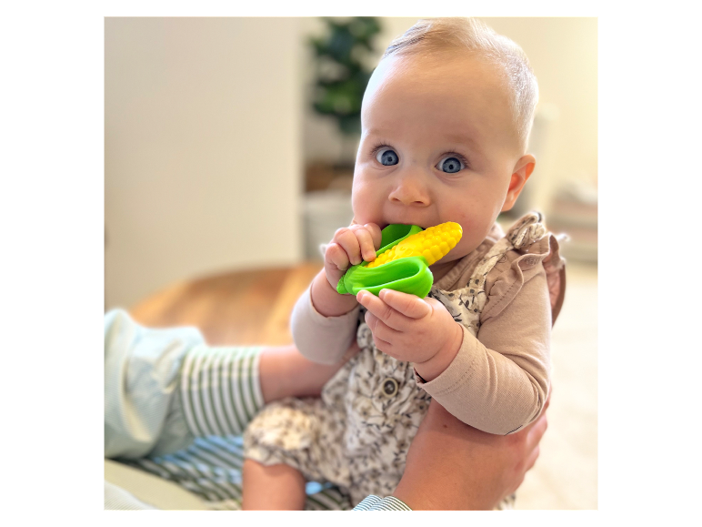 Bébé tenant un jouet en forme d'épi de maïs.