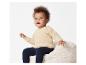 Un bébé assis sur un pouf moelleux porte un pull crème et un legging bleu marine.