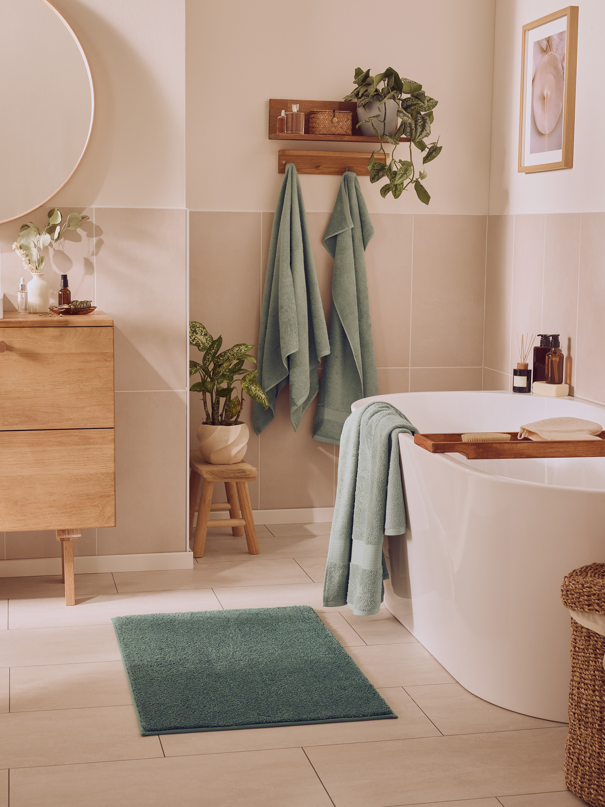 Salle de bain moderne avec baignoire blanche, serviettes vertes, meubles en bois et plantes.