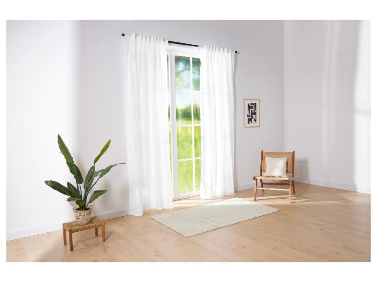 De longs rideaux blancs et un fauteuil en rotin dans une pièce lumineuse.