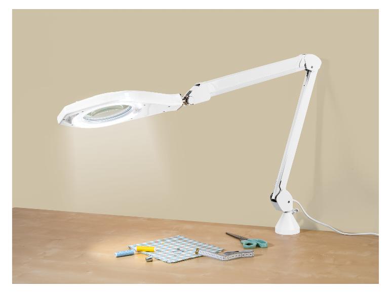 Lampe loupe blanche avec accessoires de couture sur une table en bois.