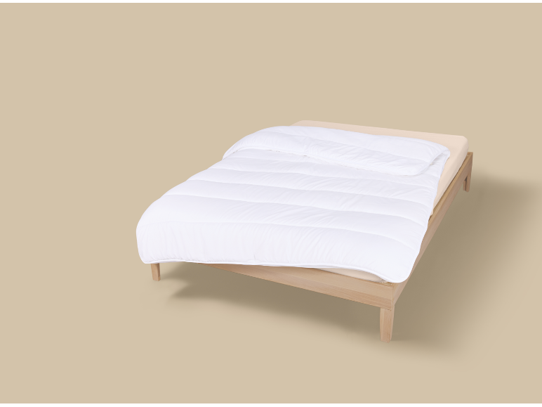Lit simple avec couette blanche et drap beige sur fond neutre.