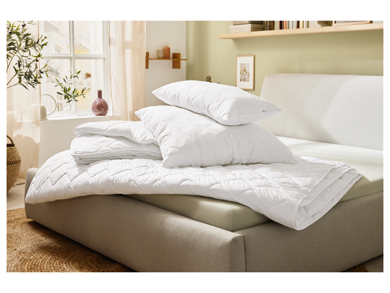 Oreillers et couettes blancs matelassés sur un lit.
