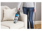 Une personne utilise un aspirateur Bissell Featherweight sur un canapé beige.