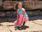 Une femme en leggings roses et un débardeur bleu attache ses chaussures de sport.