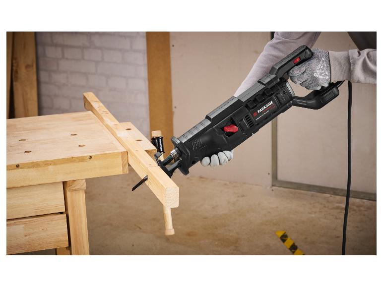 Scie Parkside Performance coupant du bois sur un établi, avec des gants.