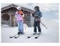 Enfants en vestes de ski CRIVIT sur la neige devant un chalet en bois.
