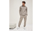 Un homme porte un sweat-shirt gris à capuche et un pantalon de survêtement avec des baskets blanches.