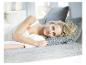 Une femme est allongée dans un lit avec une couette blanche et un oreiller gris.