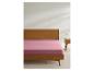 Drap rose sur lit en bois avec table de chevet et lampe.