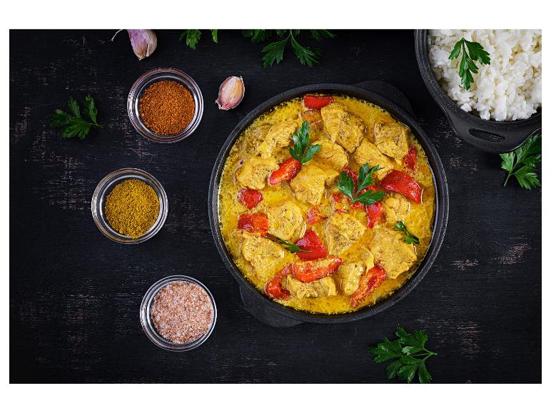 Curry de poulet aux poivrons rouges, riz et épices sur une table en bois sombre.