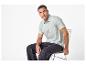 Homme en polo vert clair et jean foncé assis sur une chaise.