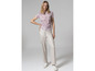 Une femme porte un t-shirt rose clair à motif et un pantalon blanc.