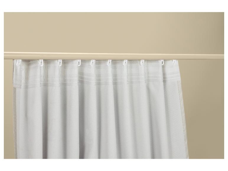 Rideaux blancs avec crochets sur une tringle à rideaux devant un mur beige.