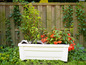 Une jardinière blanche avec une plante verte et des fleurs orange devant une clôture en bois