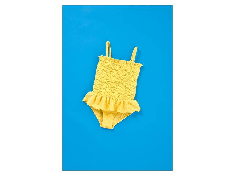 Maillot de bain jaune pour enfant avec volants sur fond bleu.