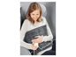 Une femme assise sur une chaise avec un coussin chauffant sur ses genoux.