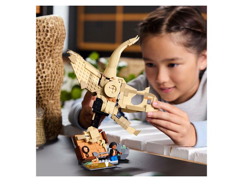 Une fille assemble un squelette de dinosaure LEGO, avec une figurine LEGO à côté d'elle.