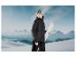 Une femme portant une veste noire et des lunettes de ski tenant des skis blancs devant une montagne.