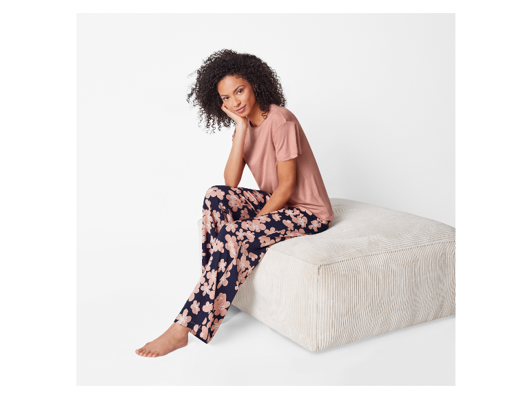 Modèle portant un pyjama fleuri et un t-shirt rose assis sur un pouf.