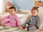 Deux bébés en pyjamas rayés et roses assis sur un lit.
