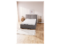 Lit avec matelas et sommier tapissier gris clair, sur sol en bois clair.