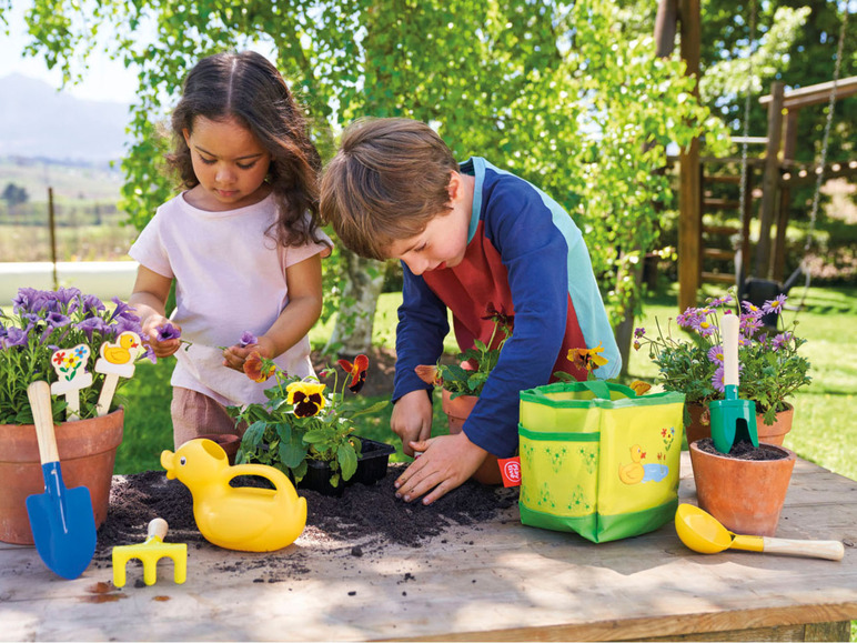 Deux enfants jouent au jardinier avec des outils jouets et des plantes en pots.
