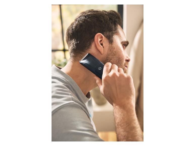 Homme utilisant une tondeuse à cheveux noire pour se raser la nuque.