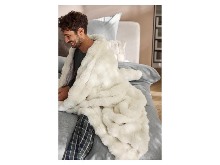 Homme en pyjama enveloppé dans une couverture premium LIVARNO® sur un lit.