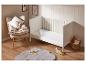 Un lit bébé blanc avec un tapis en fourrure grise et des jouets en bois.