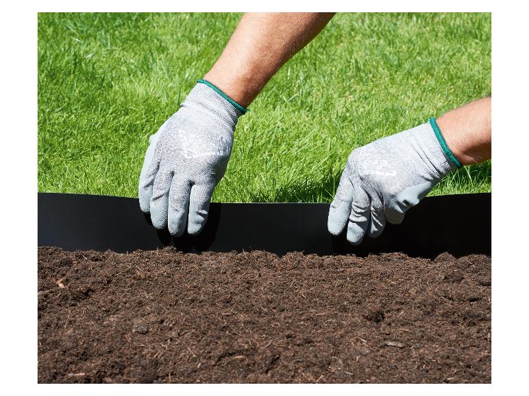 Mains gantées installant une bordure de jardin noire entre l'herbe et la terre.