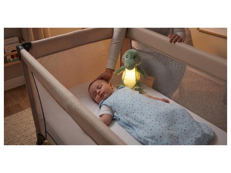 Bébé dormant dans un lit de voyage avec une veilleuse crocodile lumineuse, main du parent à proximité.