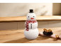 Boîte à biscuits bonhomme de neige avec chapeau et écharpe, à côté d'un bol de biscuits sur une table en bois.