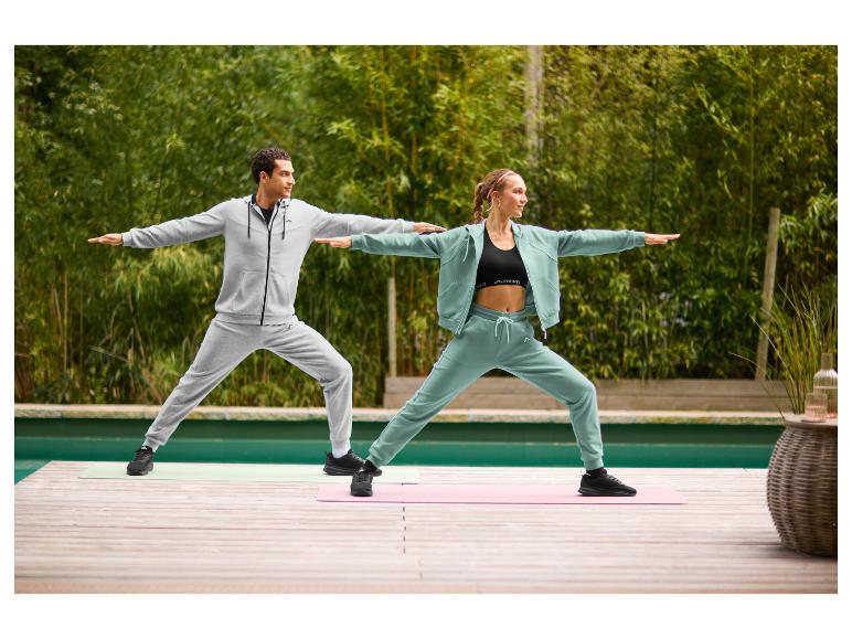 Une femme vêtue d'une veste de loisirs CRIVIT vert sauge et d'un pantalon assorti fait du yoga en plein air.