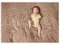 Un bébé dans un body jaune est allongé sur une couverture tricotée.