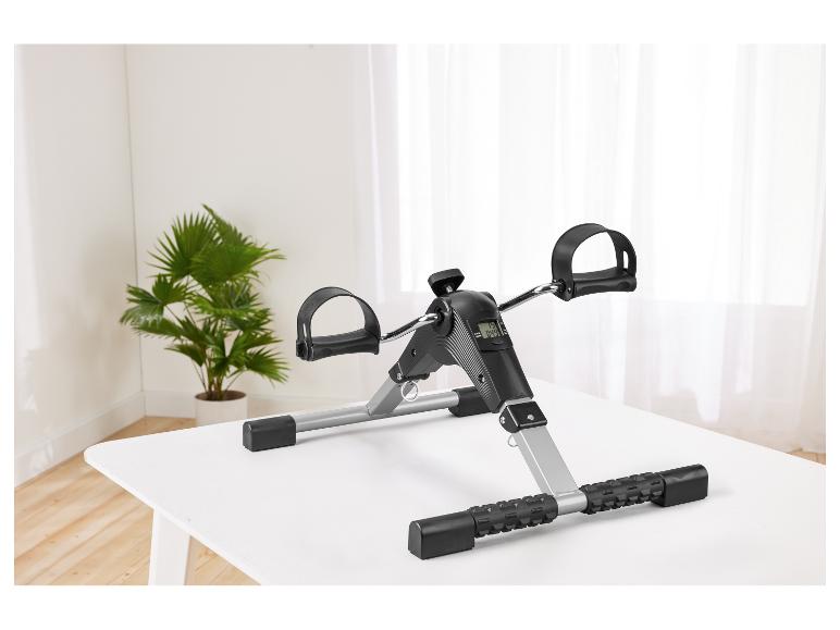 Mini vélo d'appartement avec écran numérique sur une table blanche, avec une plante en arrière-plan.