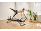 Une femme effectuant un exercice de planche avec une jambe levée sur un réformeur de pilates.