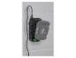 Chargeur noir avec une batterie grise attachée, monté sur un mur de briques blanches.