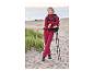 Femme en veste et pantalon de trekking rouges avec sac à dos et bâtons sur la plage.