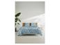 Parure de lit à motif géométrique bleu sur un lit avec tête de lit en bois, à côté d'une plante.