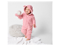 Une petite fille dans une combinaison en peluche rose joue avec une balle de baseball.