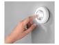 Une main active une lampe LED ronde et blanche sur un mur.