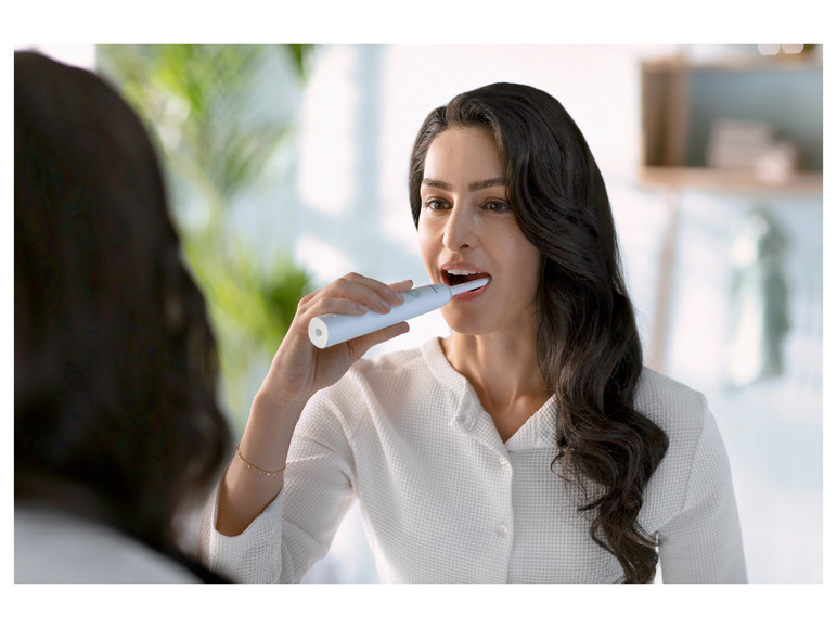 Une femme se brosse les dents avec une brosse à dents électrique Oral-B.