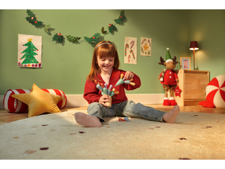 Enfant souriant jouant avec un jouet en bois sur un tapis de Noël.