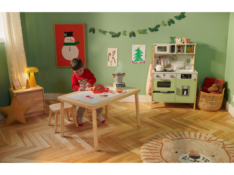 Un enfant joue avec une cuisine et une table en bois dans une pièce décorée pour Noël.