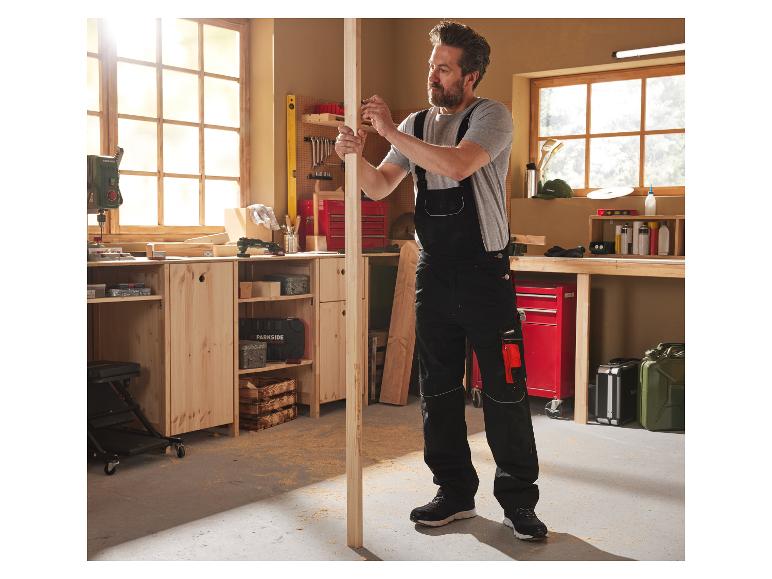 Un homme en combinaison de travail Parkside mesure un morceau de bois dans son atelier bien équipé.